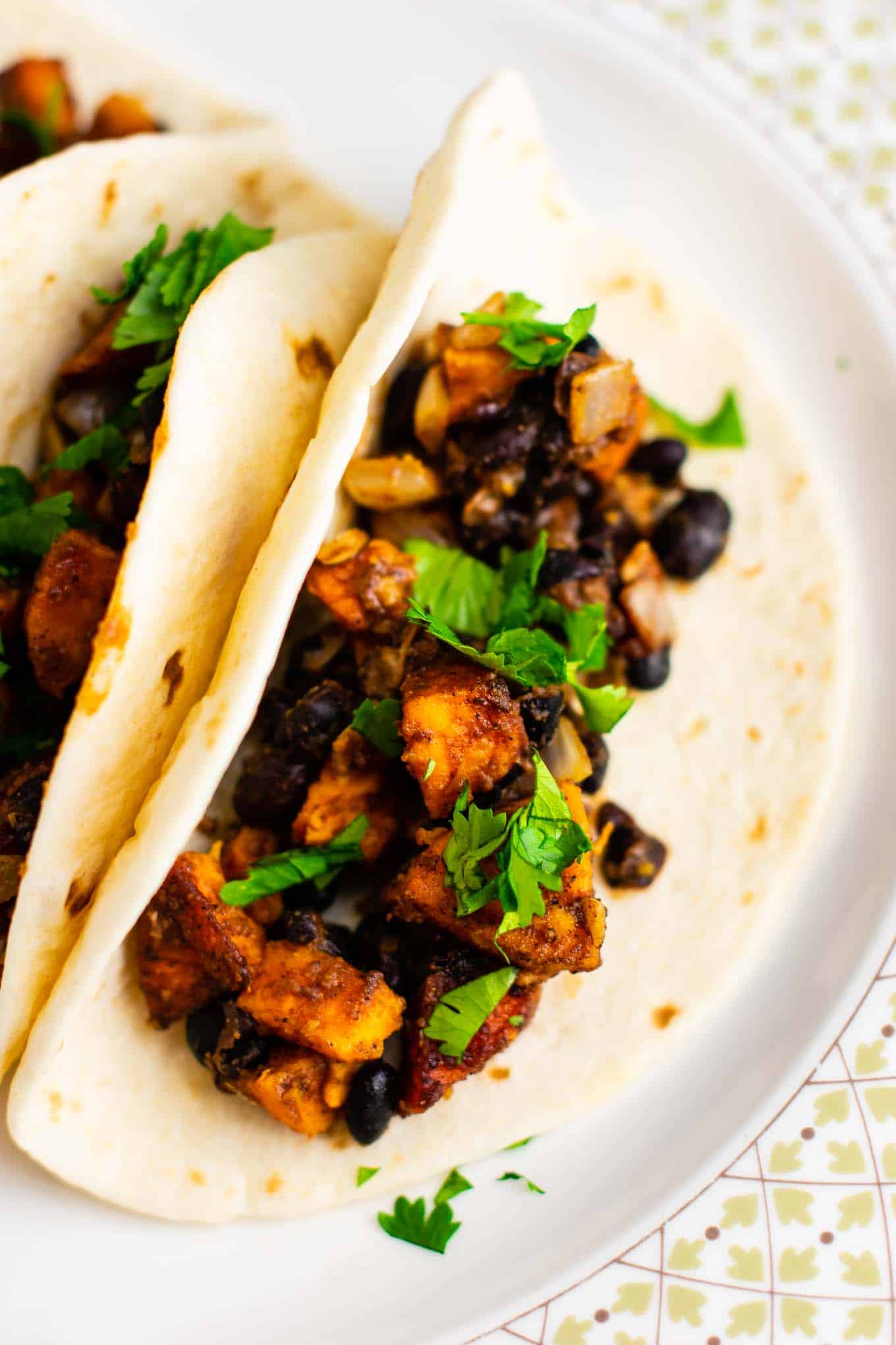Sweet potato tacos with black beans and cilantro. Healthy, meatless, insanely delicious vegan dinner recipe! Serve with salsa and optional sour cream. #vegan #sweetpotatotacos #sweetpotatorecipes #sweetpotato #veganmexican #vegandinner #vegetarian #vegetariandinner #meatlessdinner #meatlesstacos #vegantacos