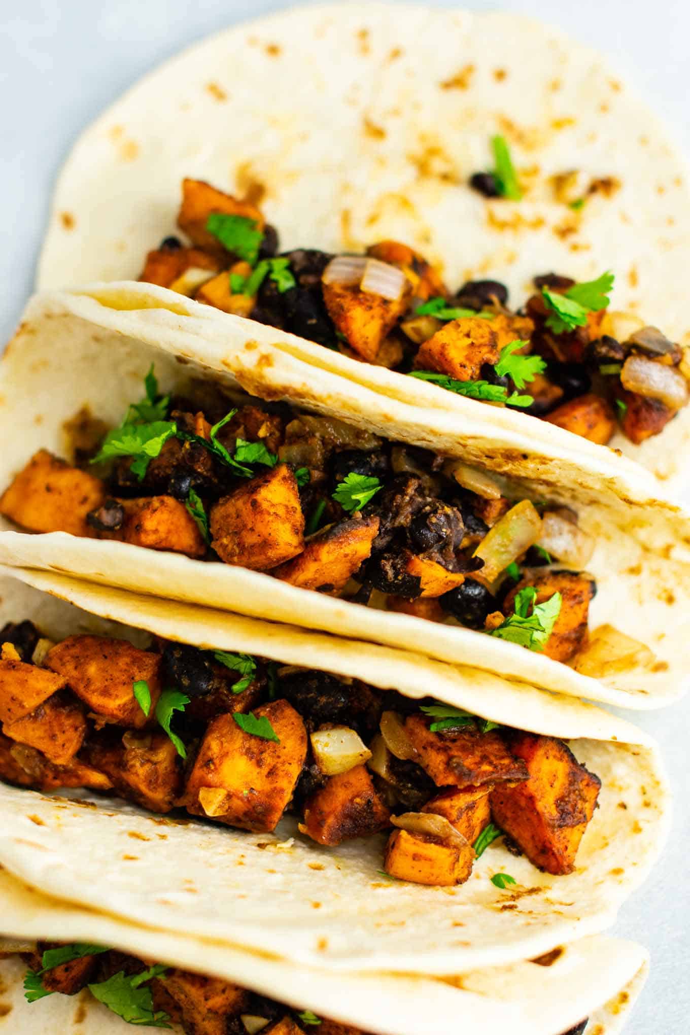 Sweet potato tacos with black beans and cilantro. Healthy, meatless, insanely delicious vegan dinner recipe! Serve with salsa and optional sour cream. #vegan #sweetpotatotacos #sweetpotatorecipes #sweetpotato #veganmexican #vegandinner #vegetarian #vegetariandinner #meatlessdinner #meatlesstacos #vegantacos