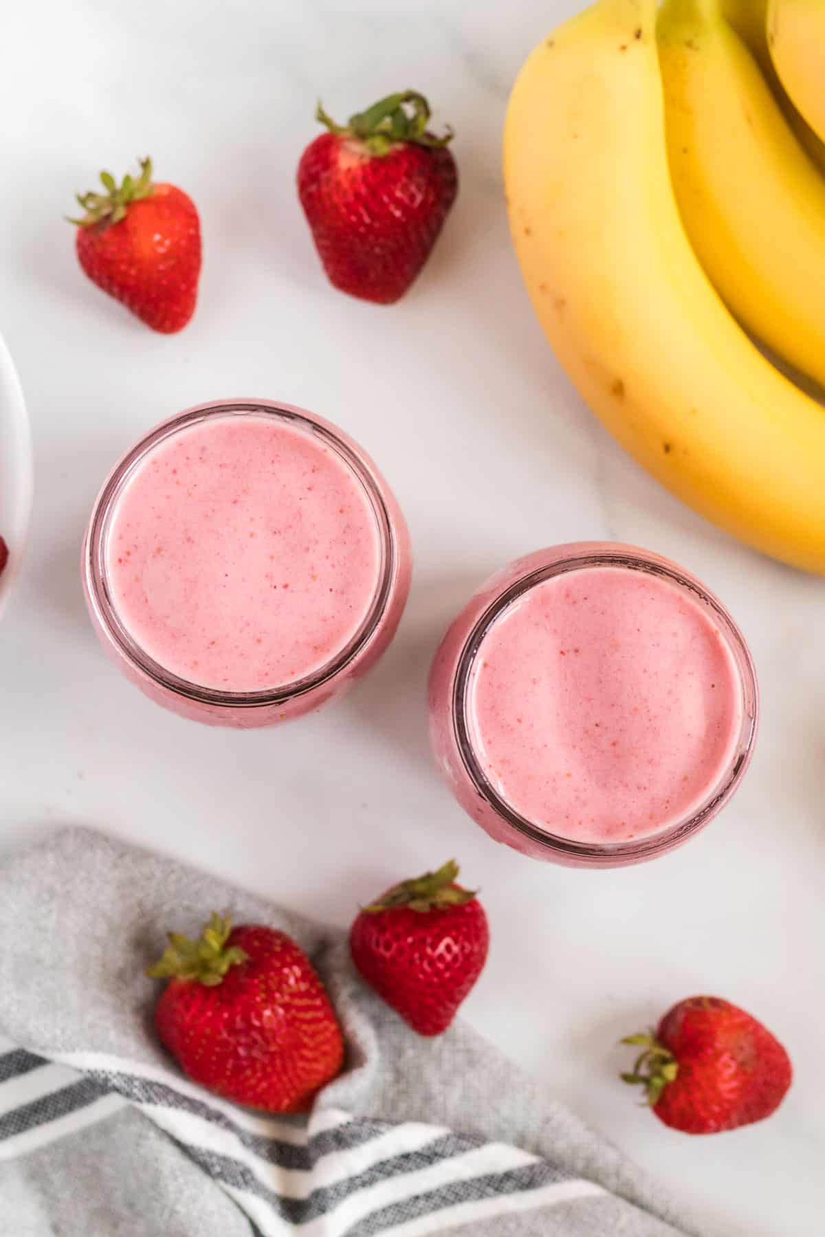 smoothies in glass jars from an overhead view surrounded by strawberries and bananas