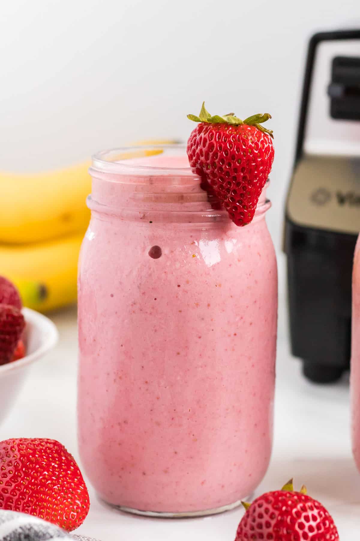 strawberry banana smoothie in a mason jar with a strawberry on the rim