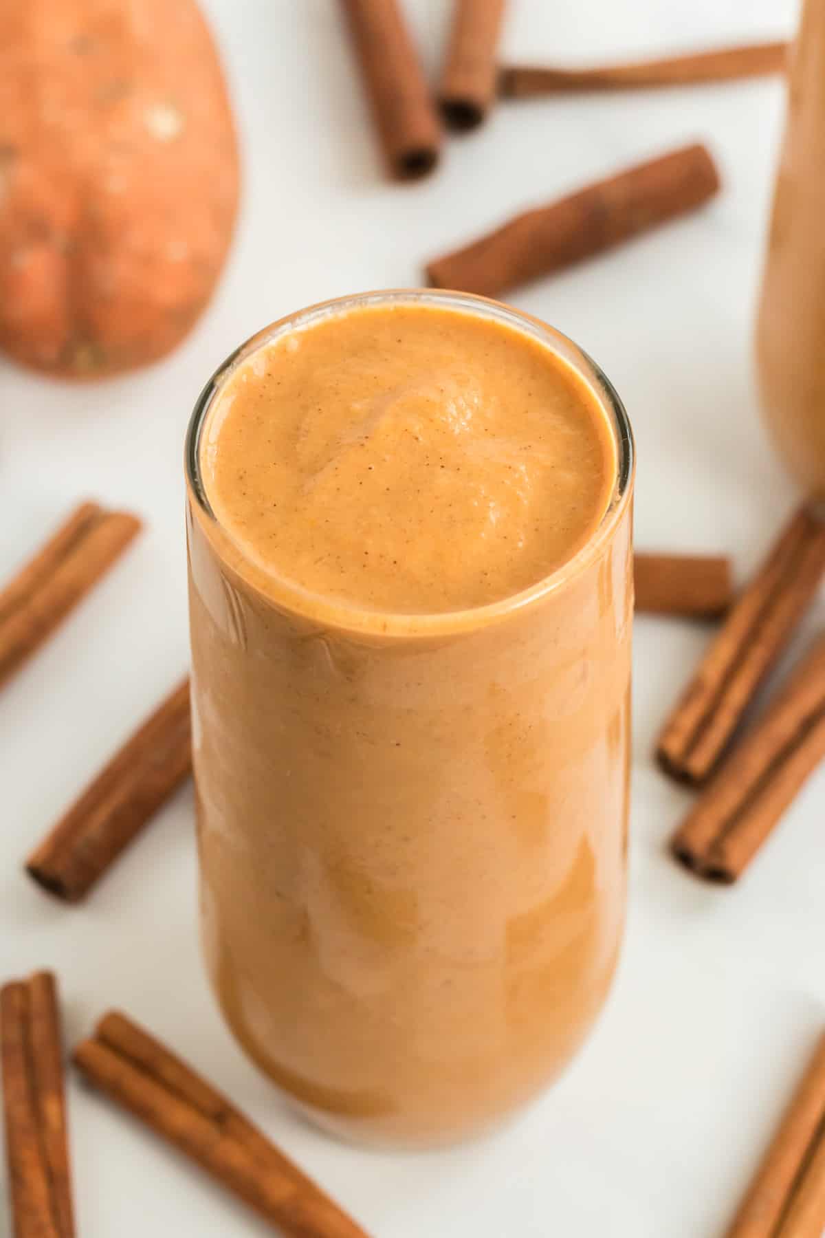 tall glass filled with sweet potato smoothie with cinnamon sticks in the background