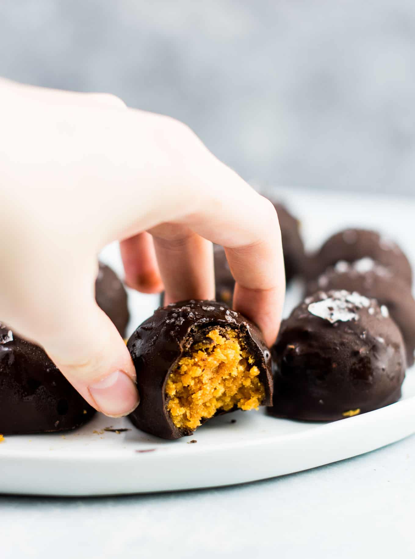 a hand reaching for a pumpkin truffle from the plate