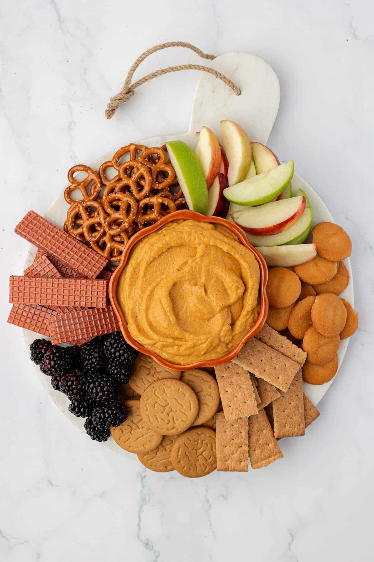 pumpkin dip on a board surrounded with crackers, apples, pretzels, and fruit