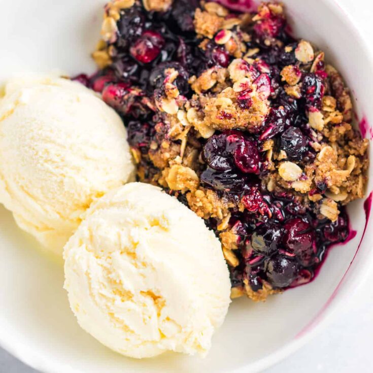 cranberry blueberry crisp in a bowl with ice cream