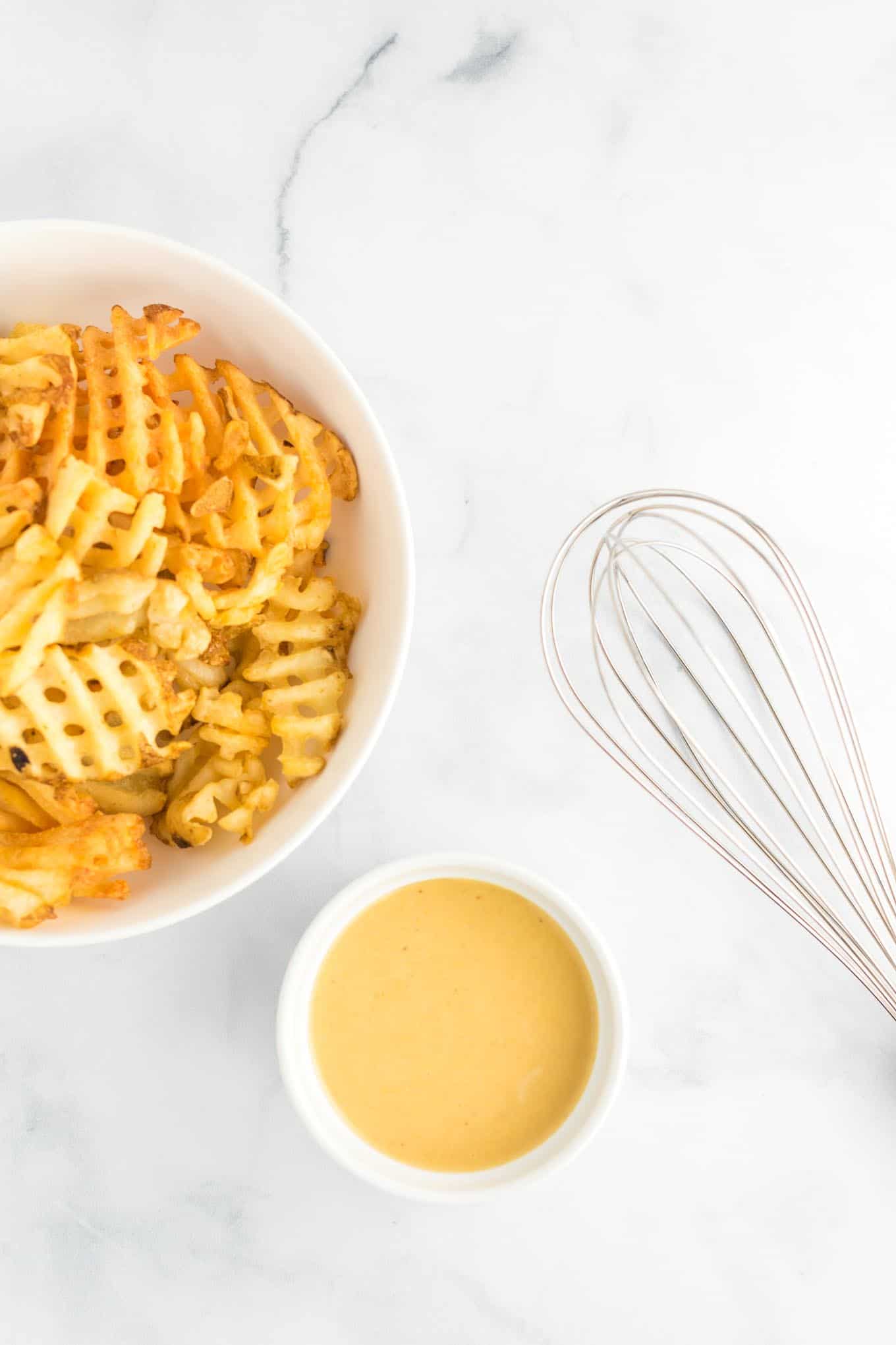 sauce in a white ramekin with fries in a bowl and a whisk