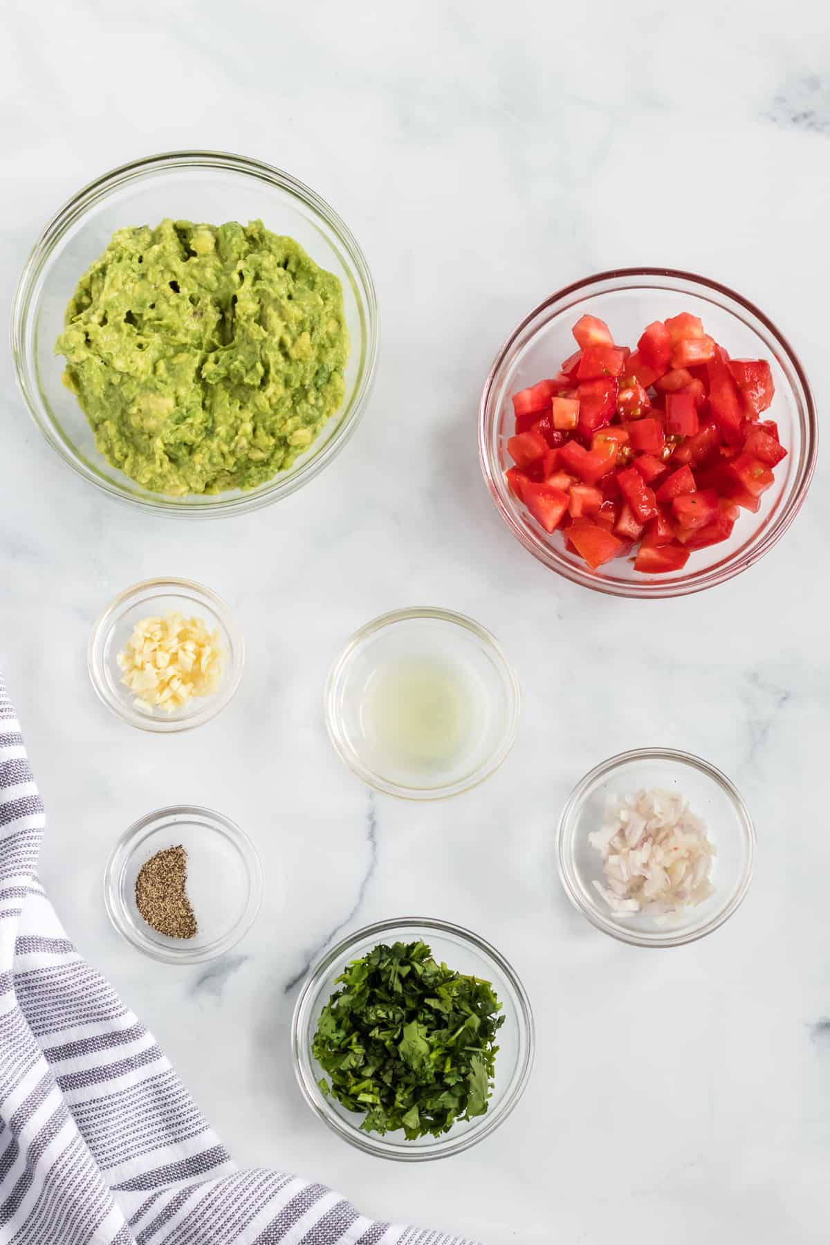 ingredients for guacamole with tomatoes in individual glass bowls