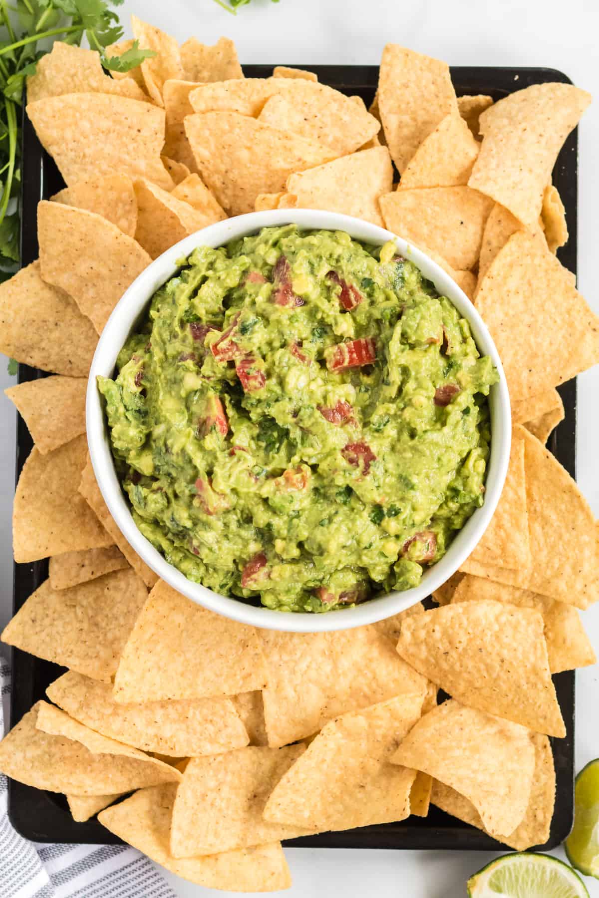 guacamole in a bowl on a platter surrounded by tortilla chips