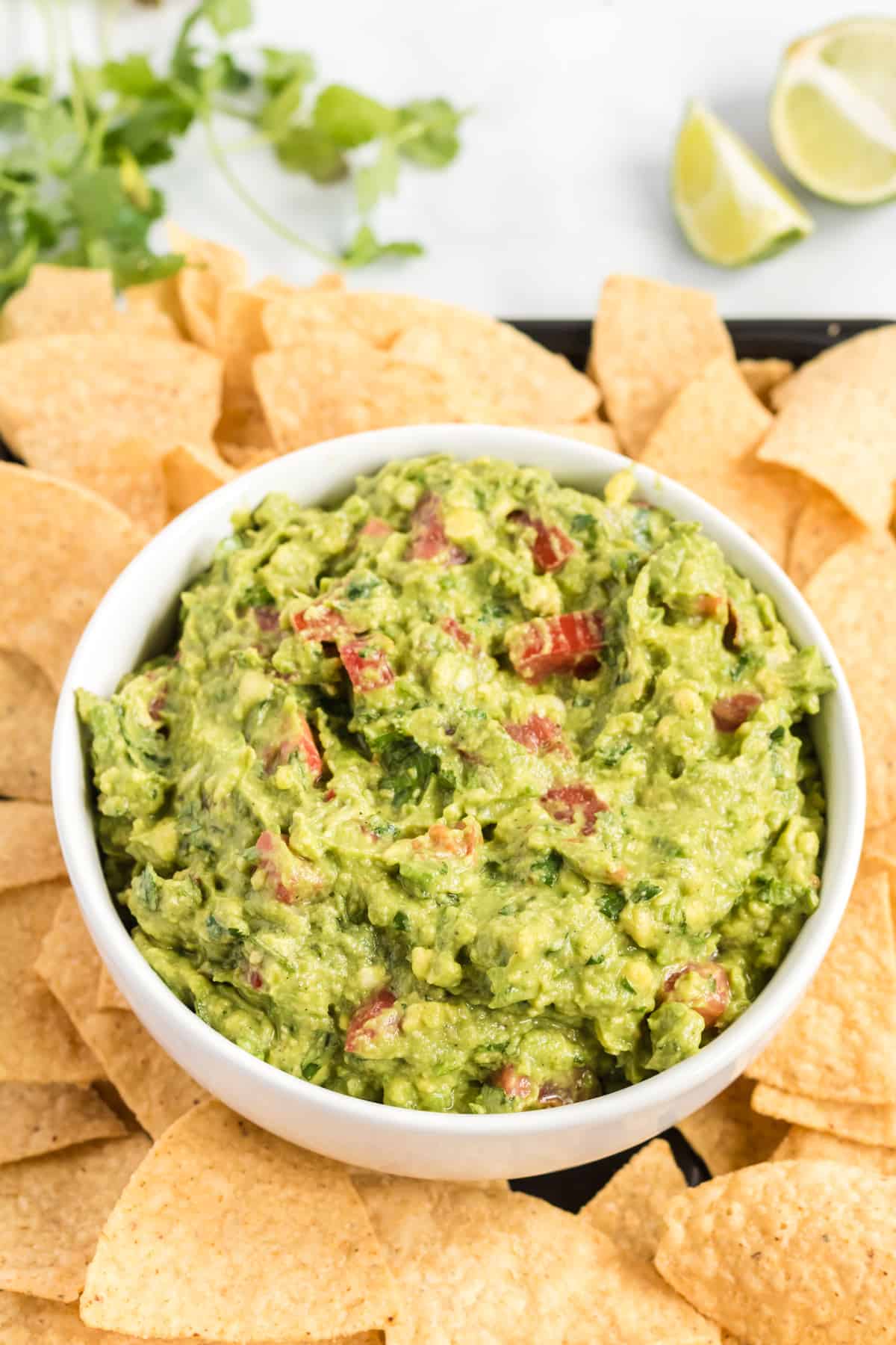 guacamole in a bowl on a platter surrounded by tortilla chips