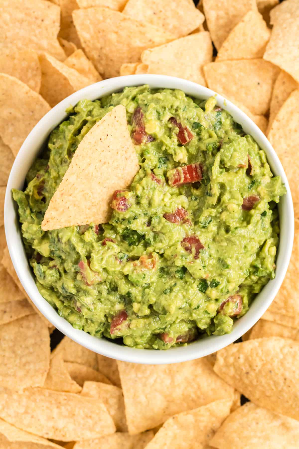 guacamole in a bowl on a platter surrounded by tortilla chips