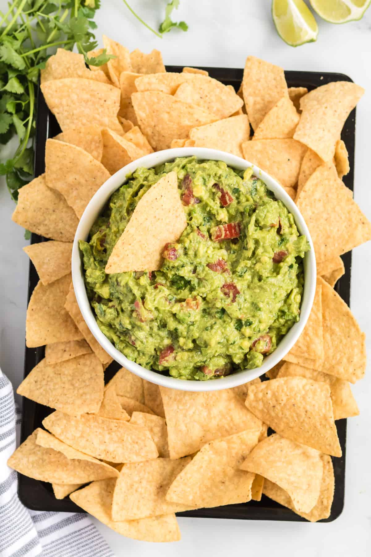 guacamole in a bowl on a platter surrounded by tortilla chips