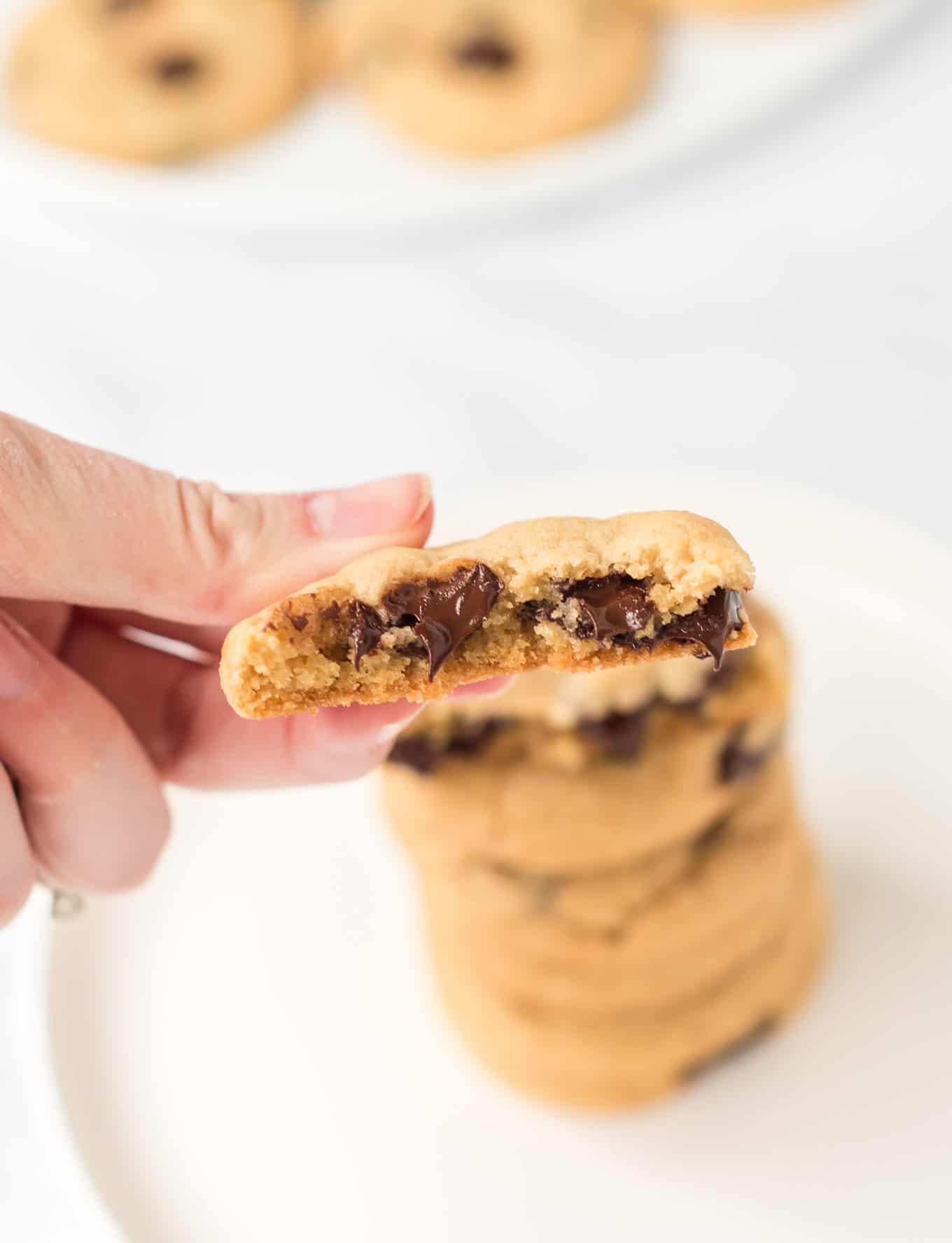a hand holding a chocolate chip cookie with a bite taken out