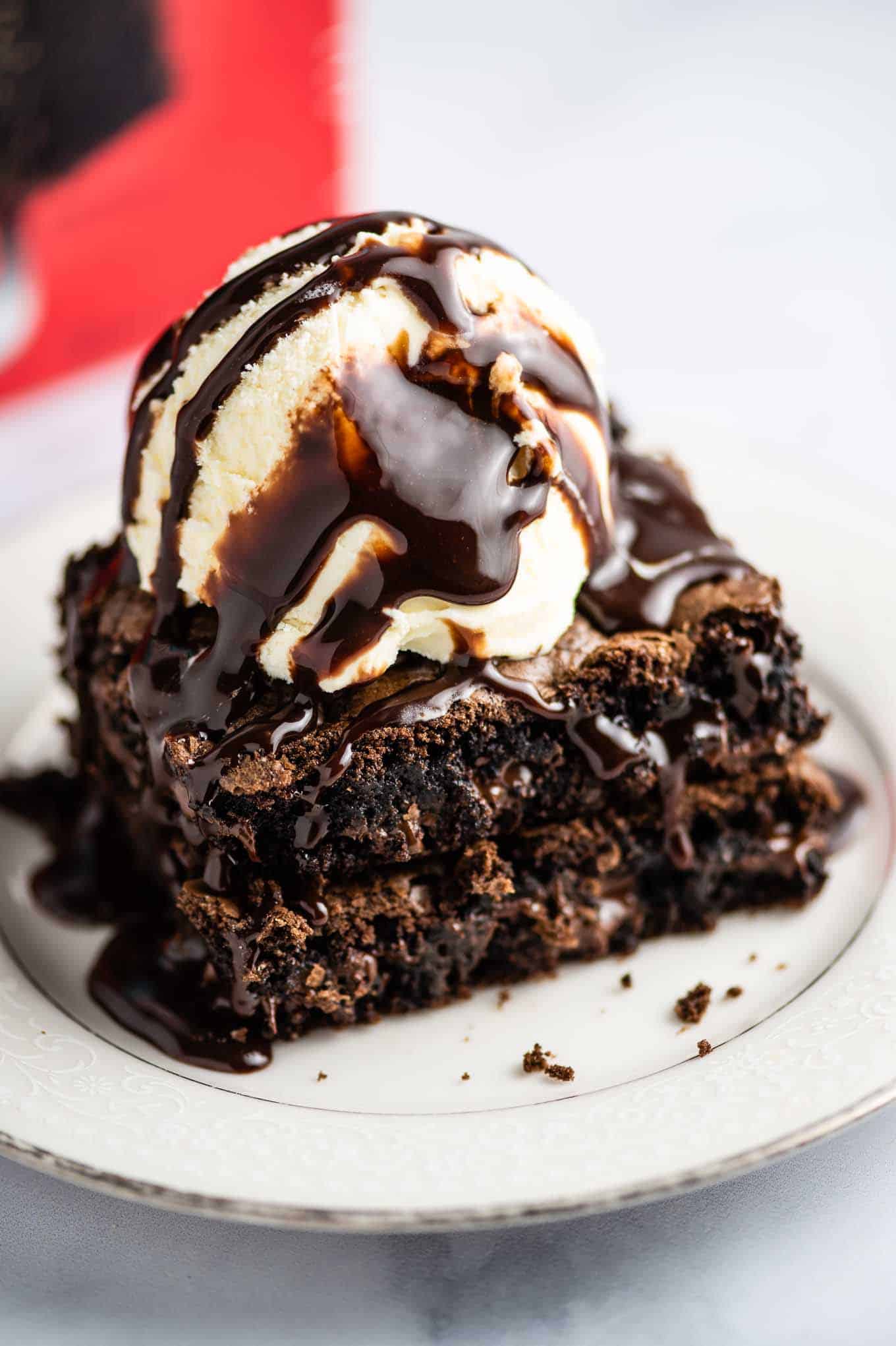 two brownies on a white plate topped with vanilla ice cream and chocolate sauce