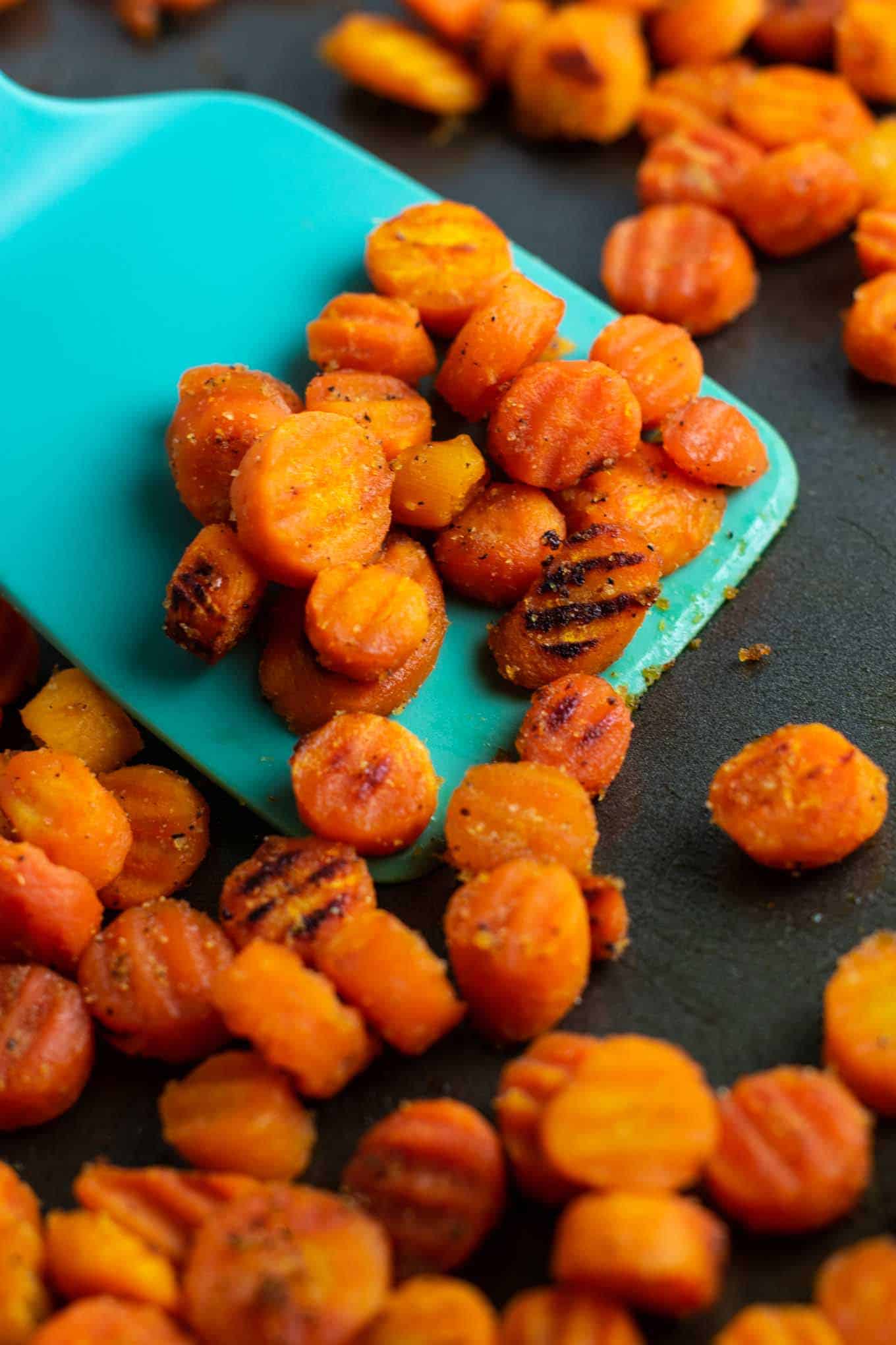 a blue spatula taking a scoop of the finished roasted frozen carrots