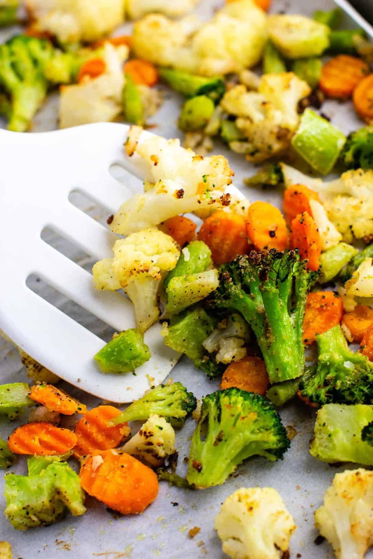 a white spatula taking a scoop of roasted vegetables