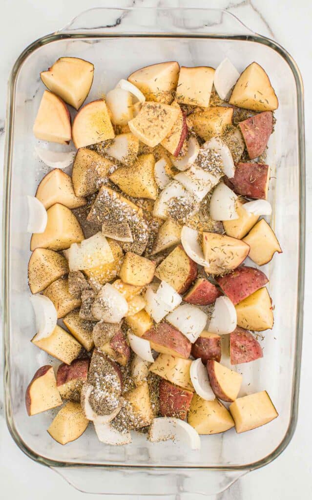 red potatoes, onions, oil, and spices in a glass baking dish