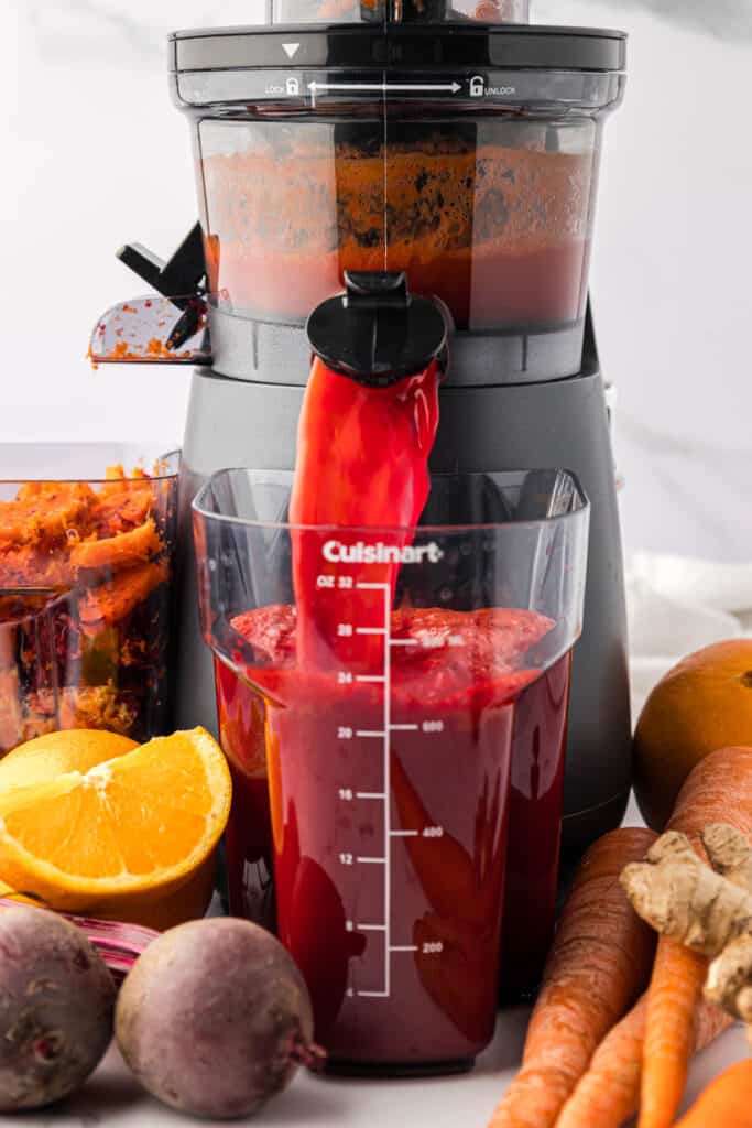 carrot beet juice pouring out of a juicer