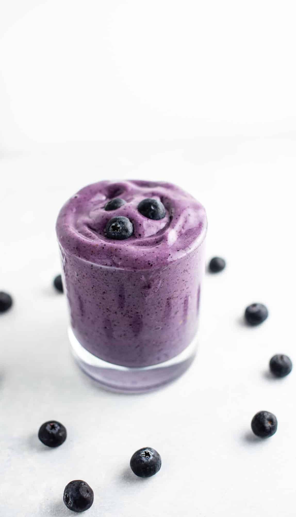 blueberry smoothie in a glass with blueberries around it