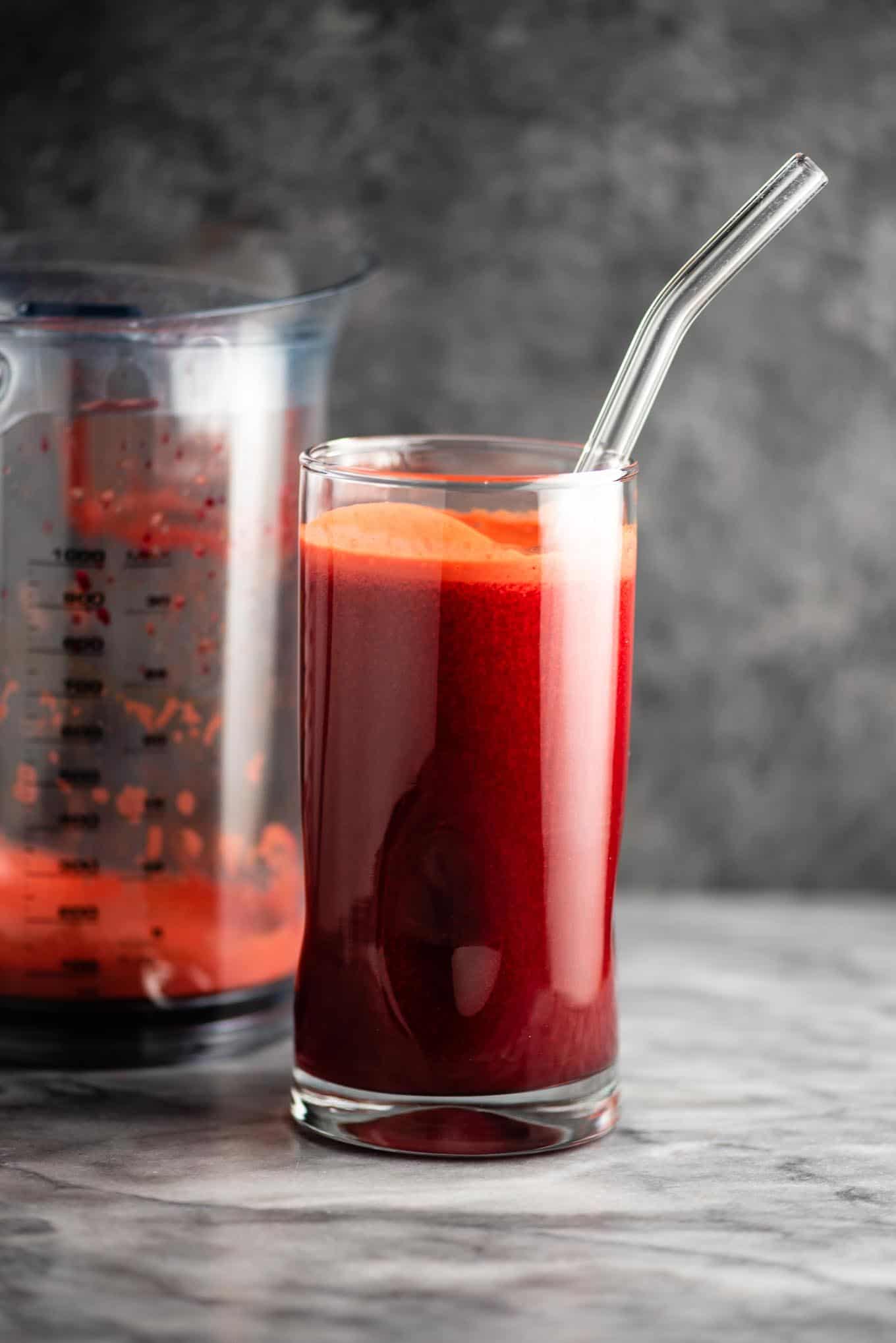 beet and carrot juice in a glass next to a juicer