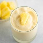 frosty pineapple smoothie in a glass with frozen pineapple on top