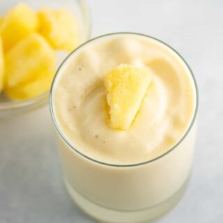 frosty pineapple smoothie in a glass with frozen pineapple on top