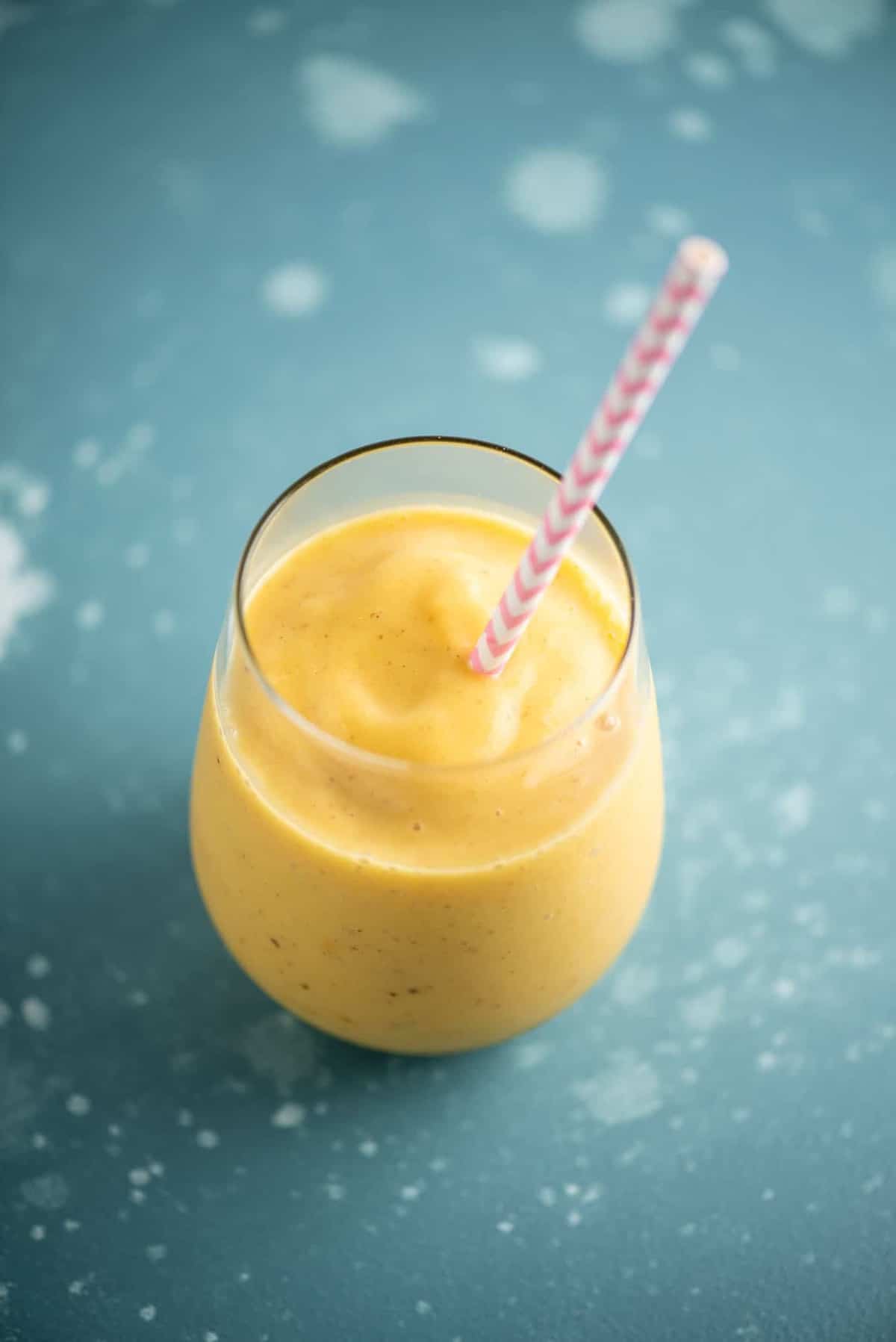 mango and pineapple smoothie in a glass with a pink straw