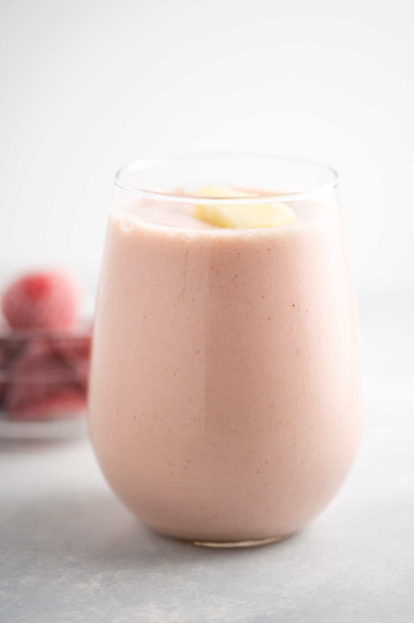 pineapple strawberry smoothie in a glass with frozen strawberries in the background