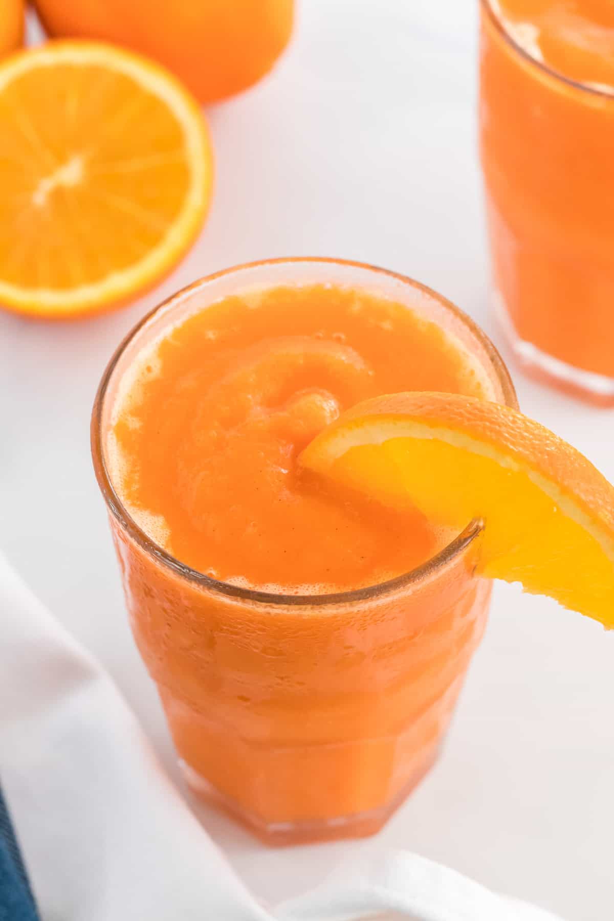 carrot orange smoothie in a glass with an orange slice on the rim