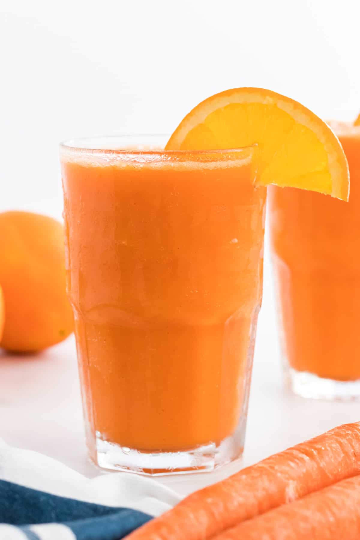 carrot smoothie in a glass with an orange slice on the rim