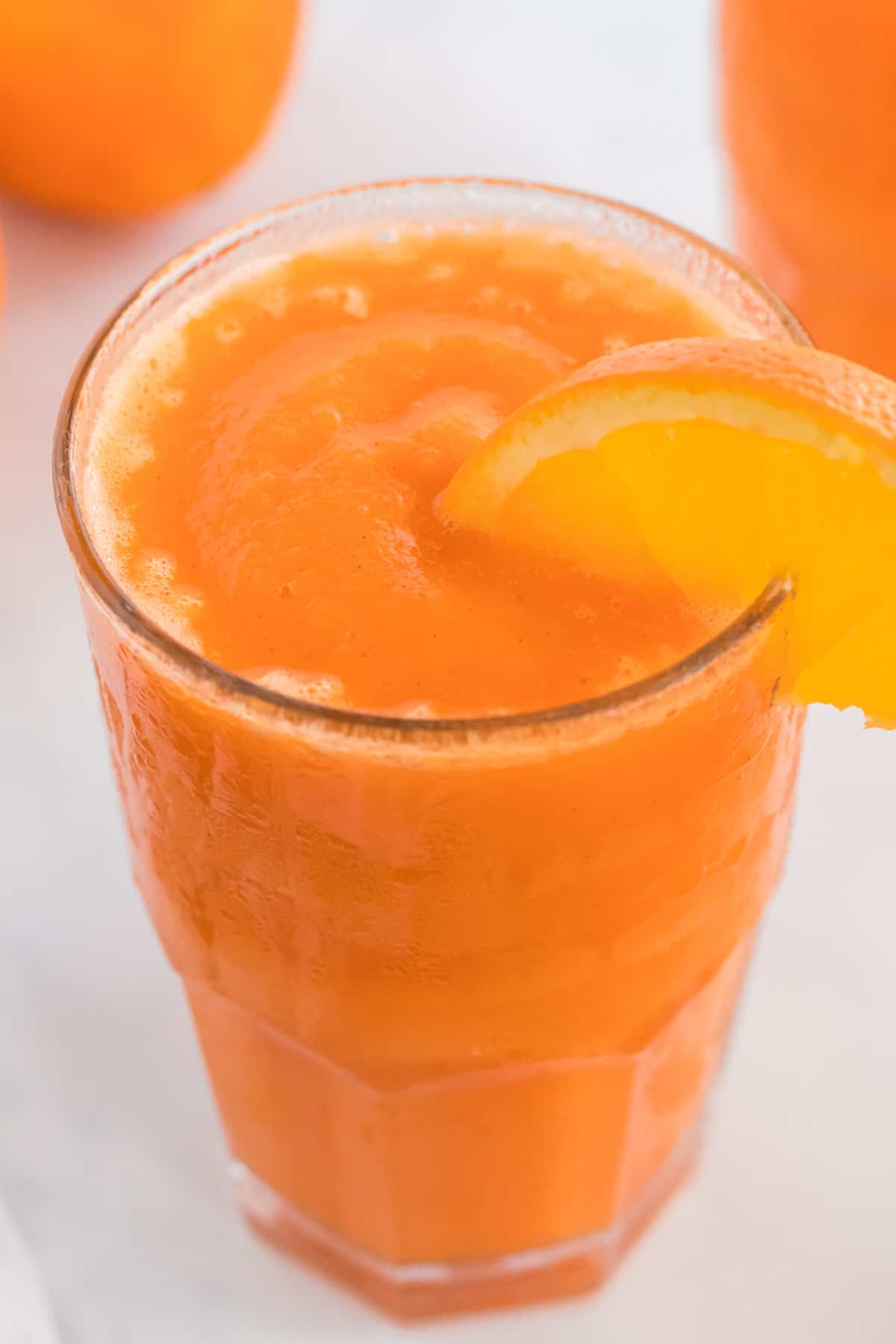 carrot smoothie in a glass with an orange slice on the rim