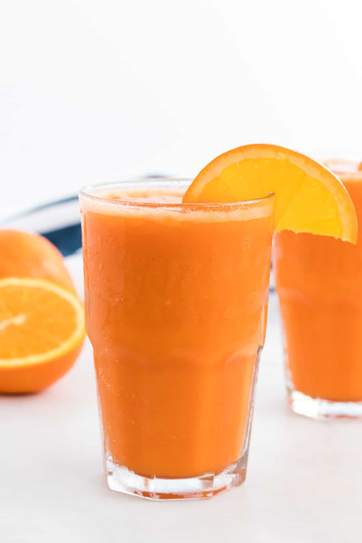 carrot orange smoothie in a glass with an orange slice on the rim