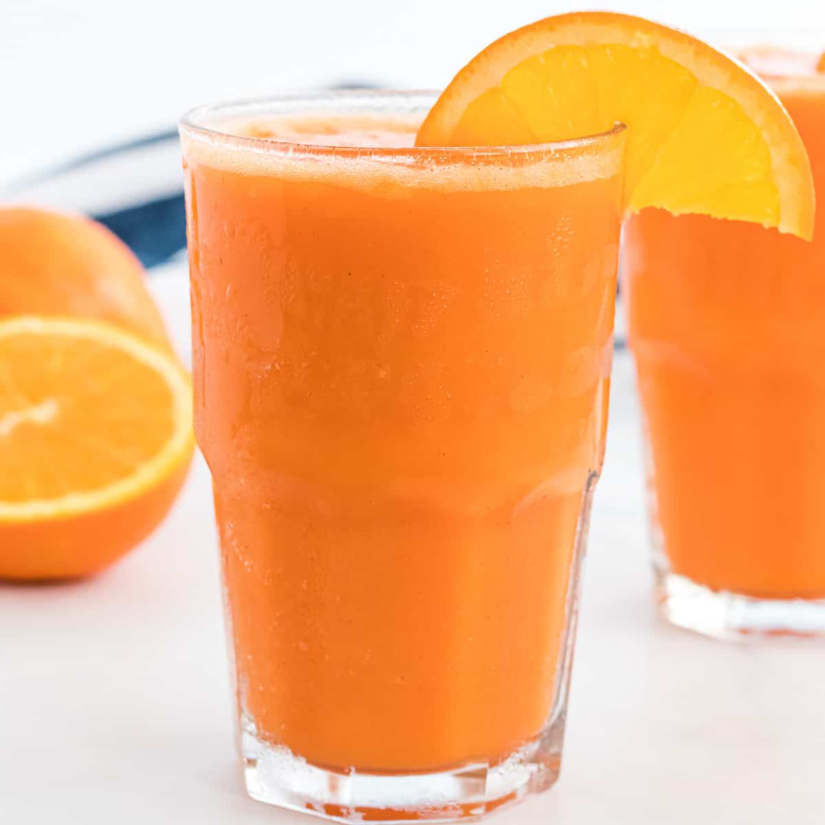 carrot orange smoothie in a glass with an orange slice on the rim