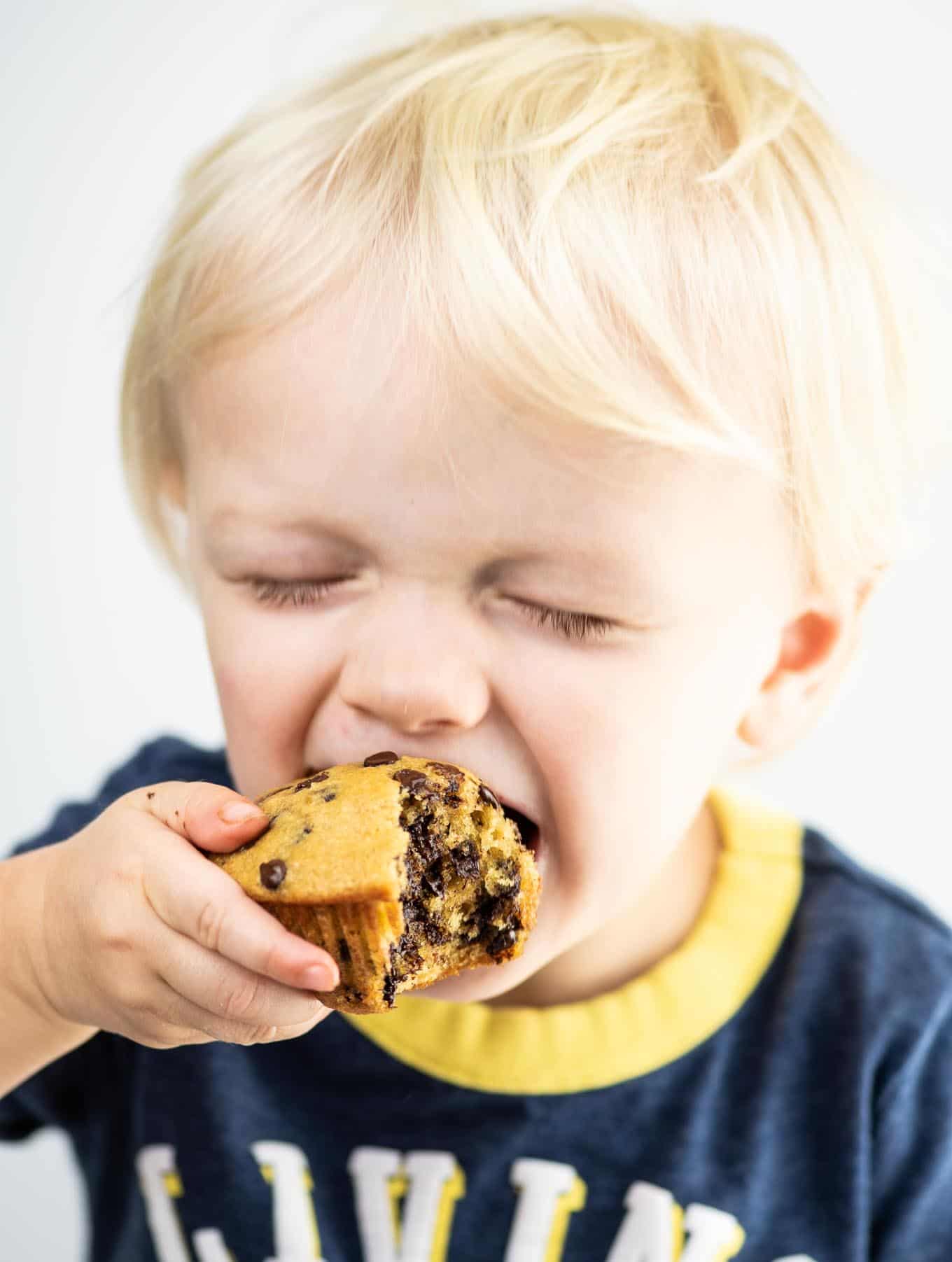 toddler taking a bite of a chocolate chip muffin