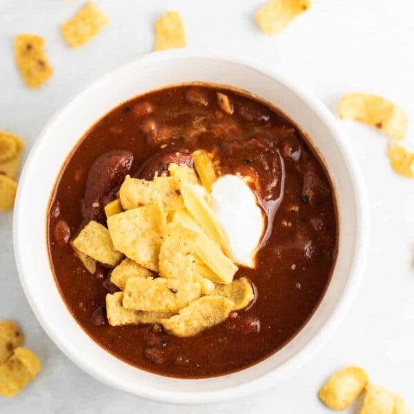 chili in a white bowl topped with sour cream and corn chips