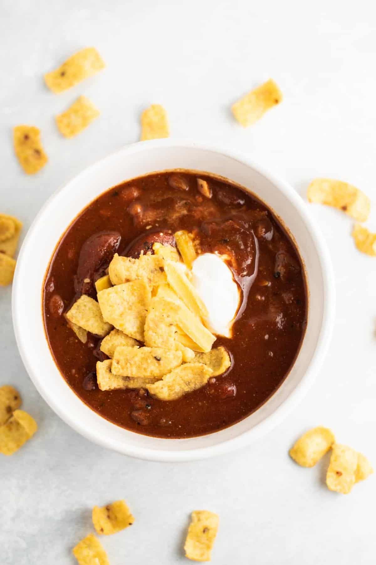 slow cooker vegetarian chili in a white bowl topped with sour cream and corn chips
