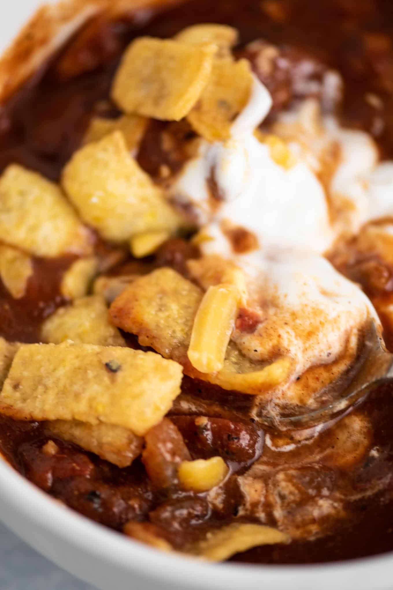 up close chili topped with sour cream, cheese, and corn chips