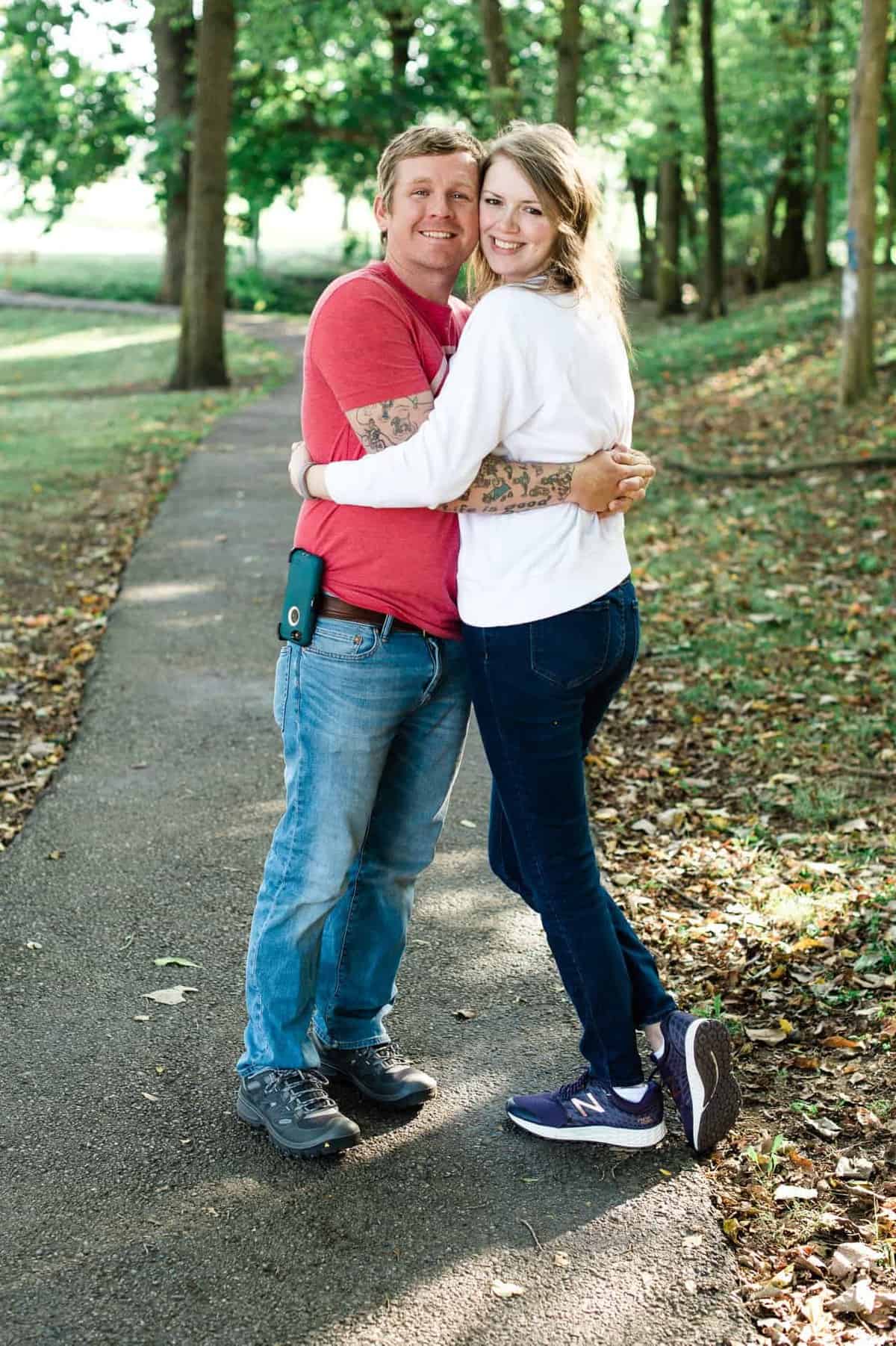 a couple hugging in a park with trees in the background