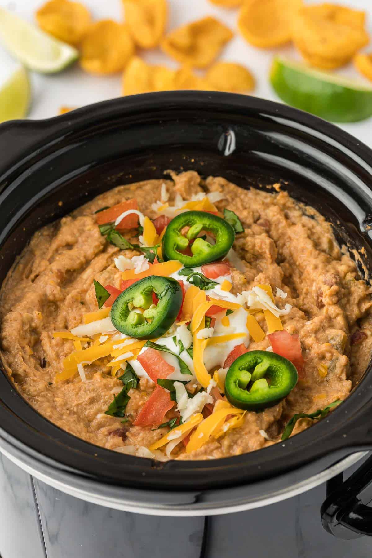 bean dip in a crock pot topped with jalapenos, cheese, and tomatoes