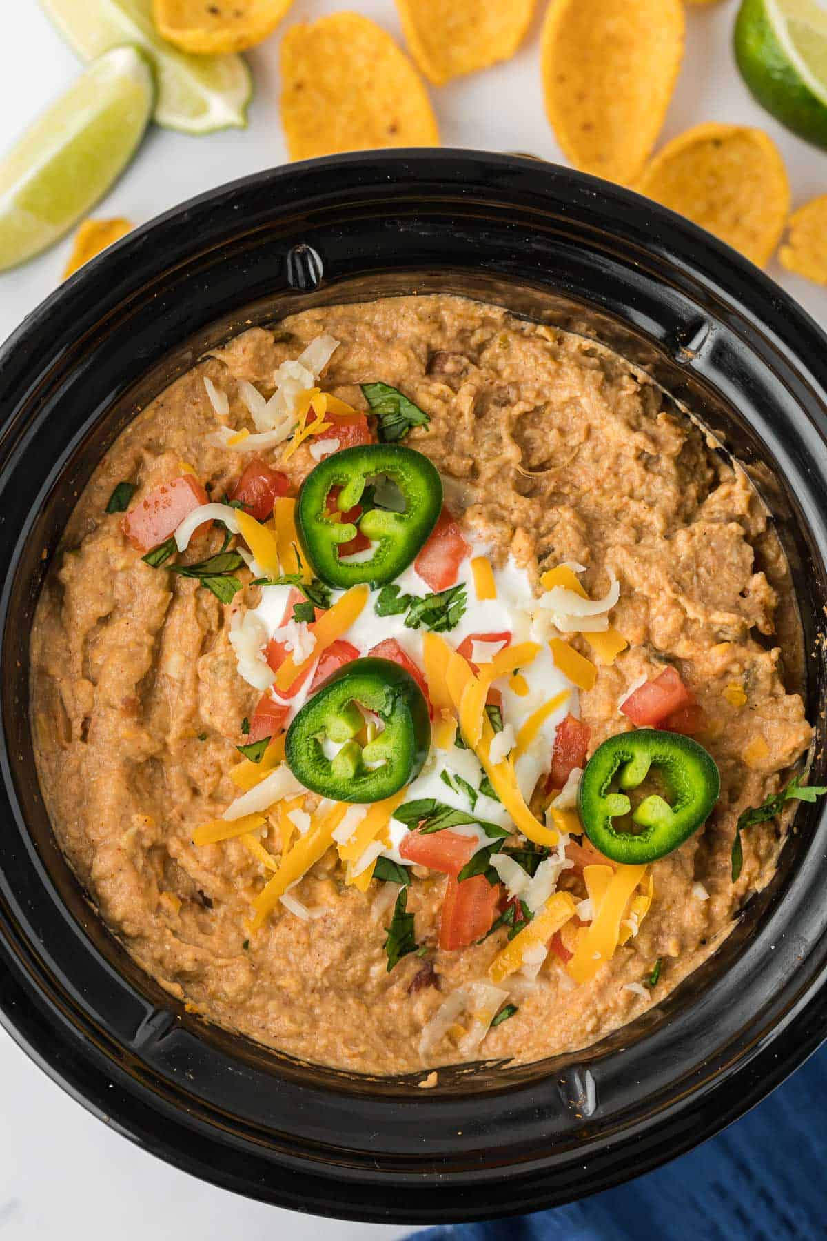 bean dip in a crock pot topped with jalapenos, cheese, and tomatoes