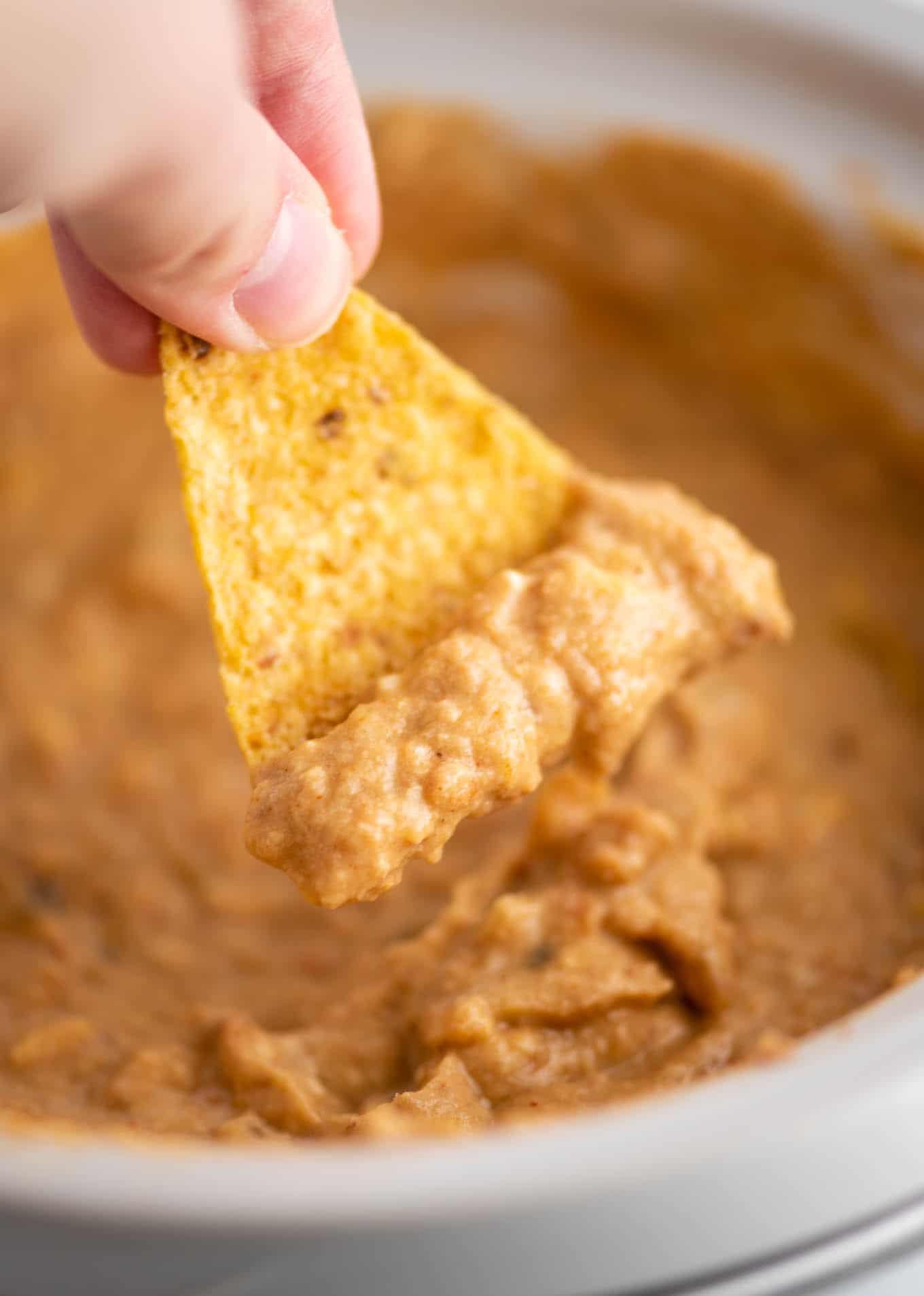 tortilla chip dipping with bean dip on it