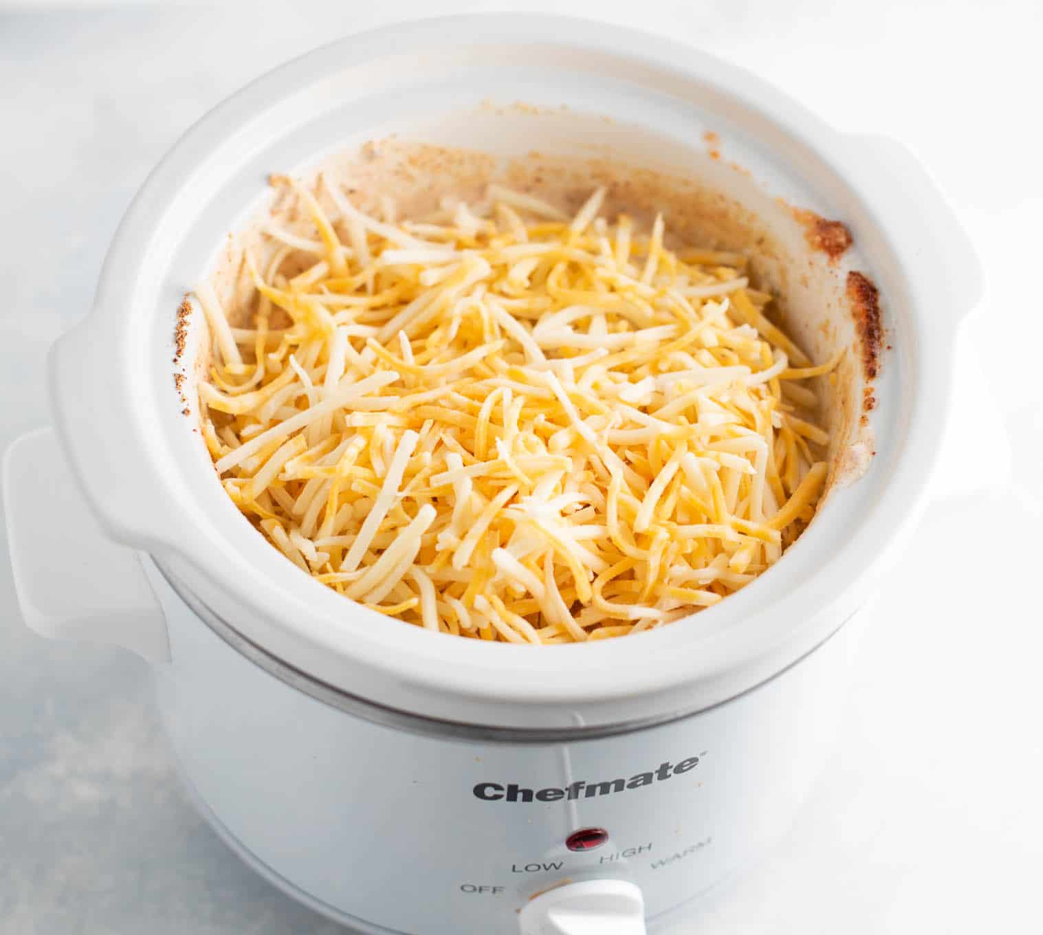 adding the mexican cheese to the bean dip on the top of the crock pot