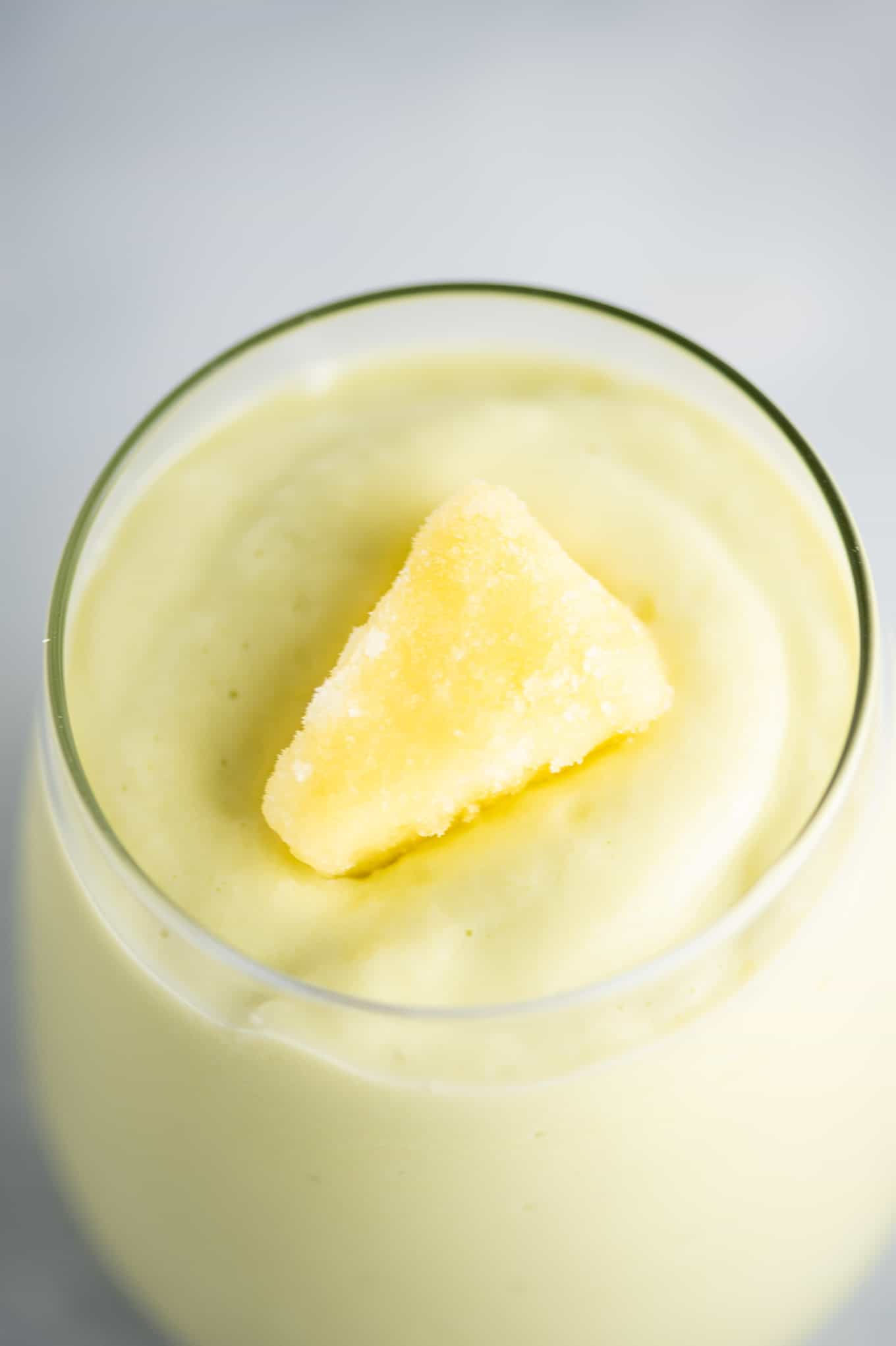avocado smoothie in a glass with a piece of frozen pineapple on top