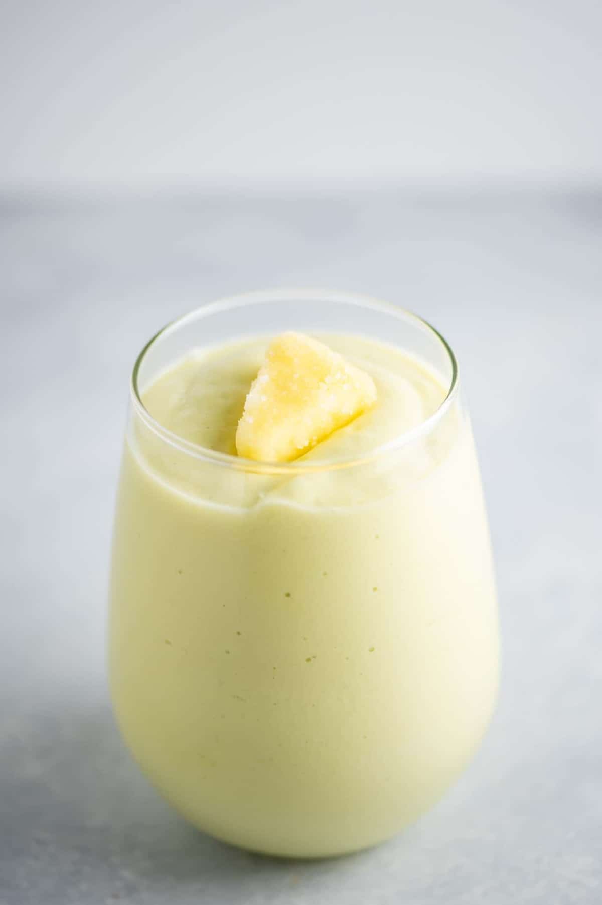 avocado smoothie in a clear glass with a piece of frozen pineapple on top