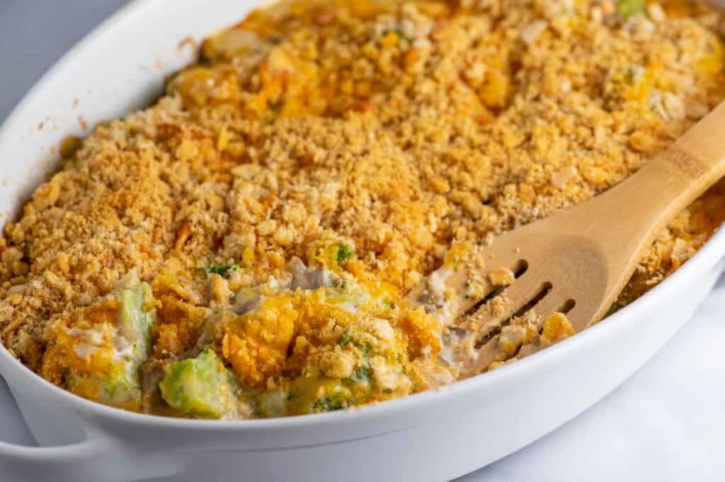 white casserole dish of broccoli casserole with a wooden serving spoon