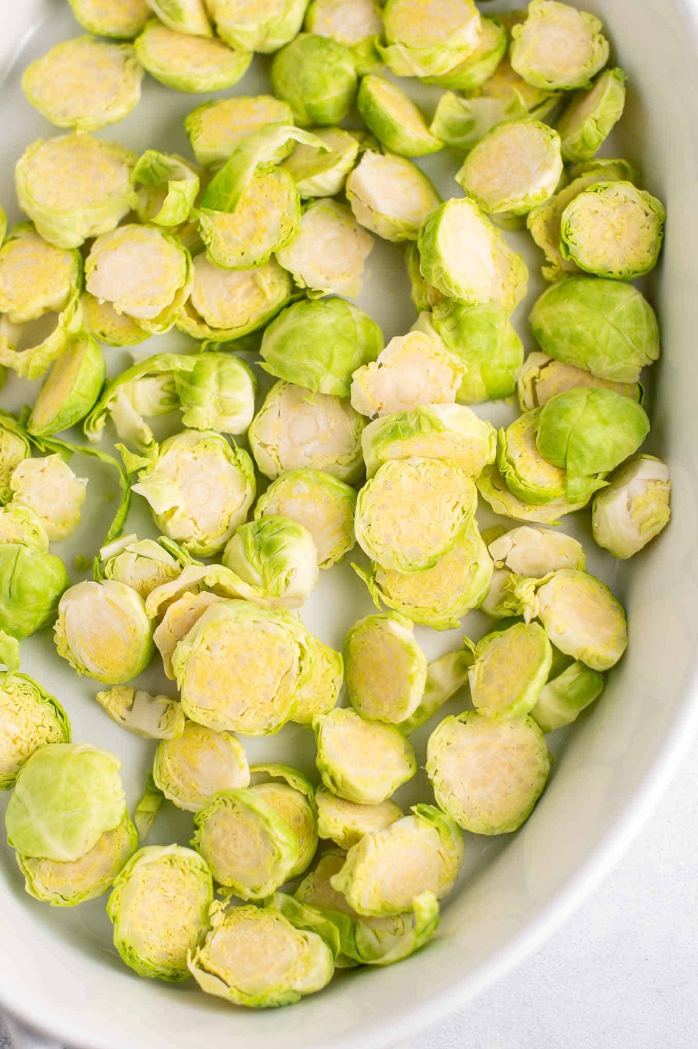 thinly sliced raw brussels sprouts in an oval white baking dish