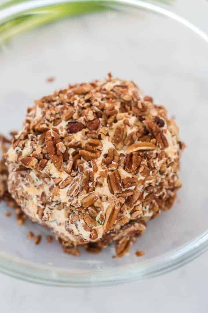cheese ball being rolled in pecans in a bowl