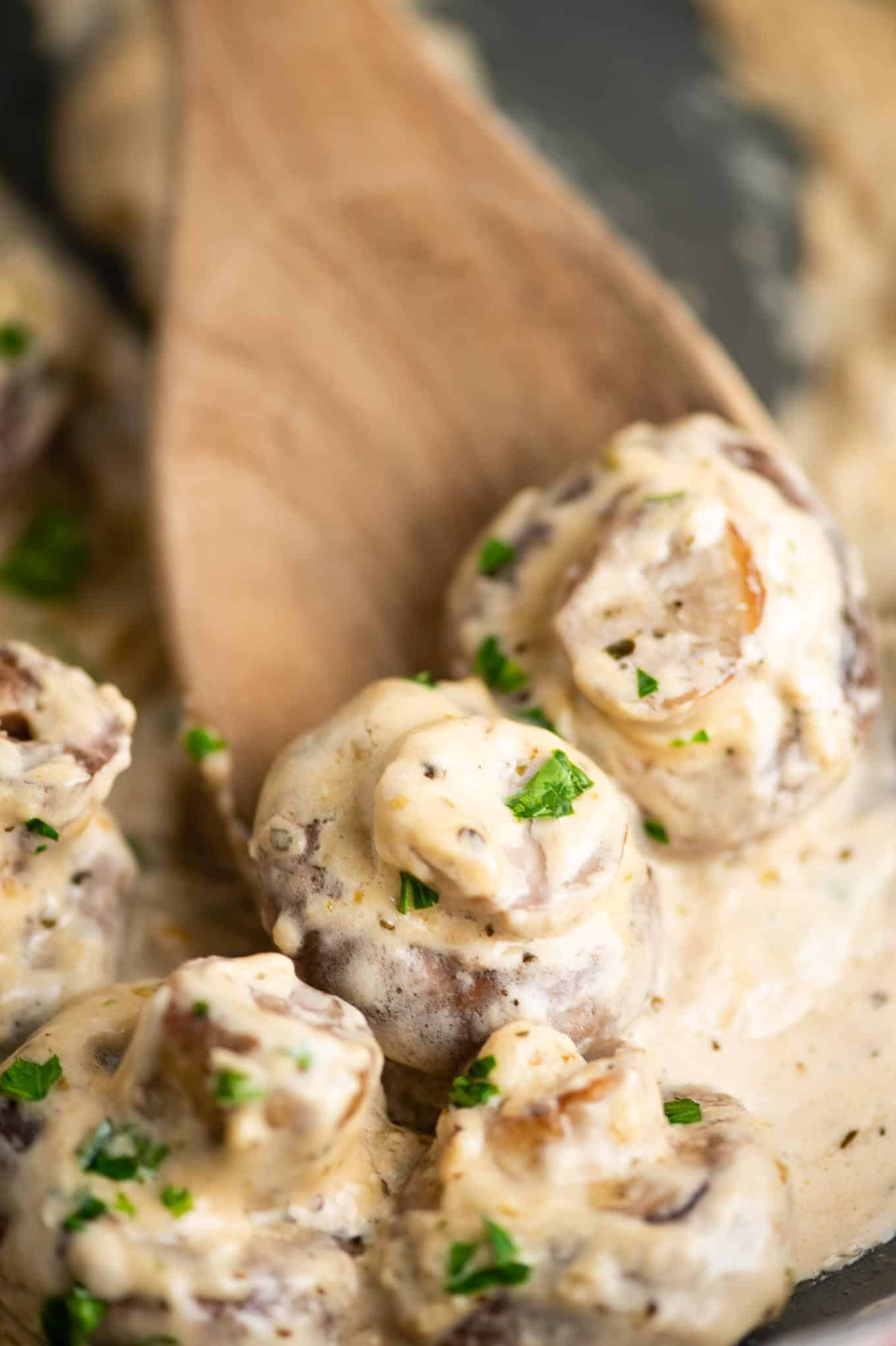 wooden spoon scooping garlic parmesan mushrooms in cream sauce