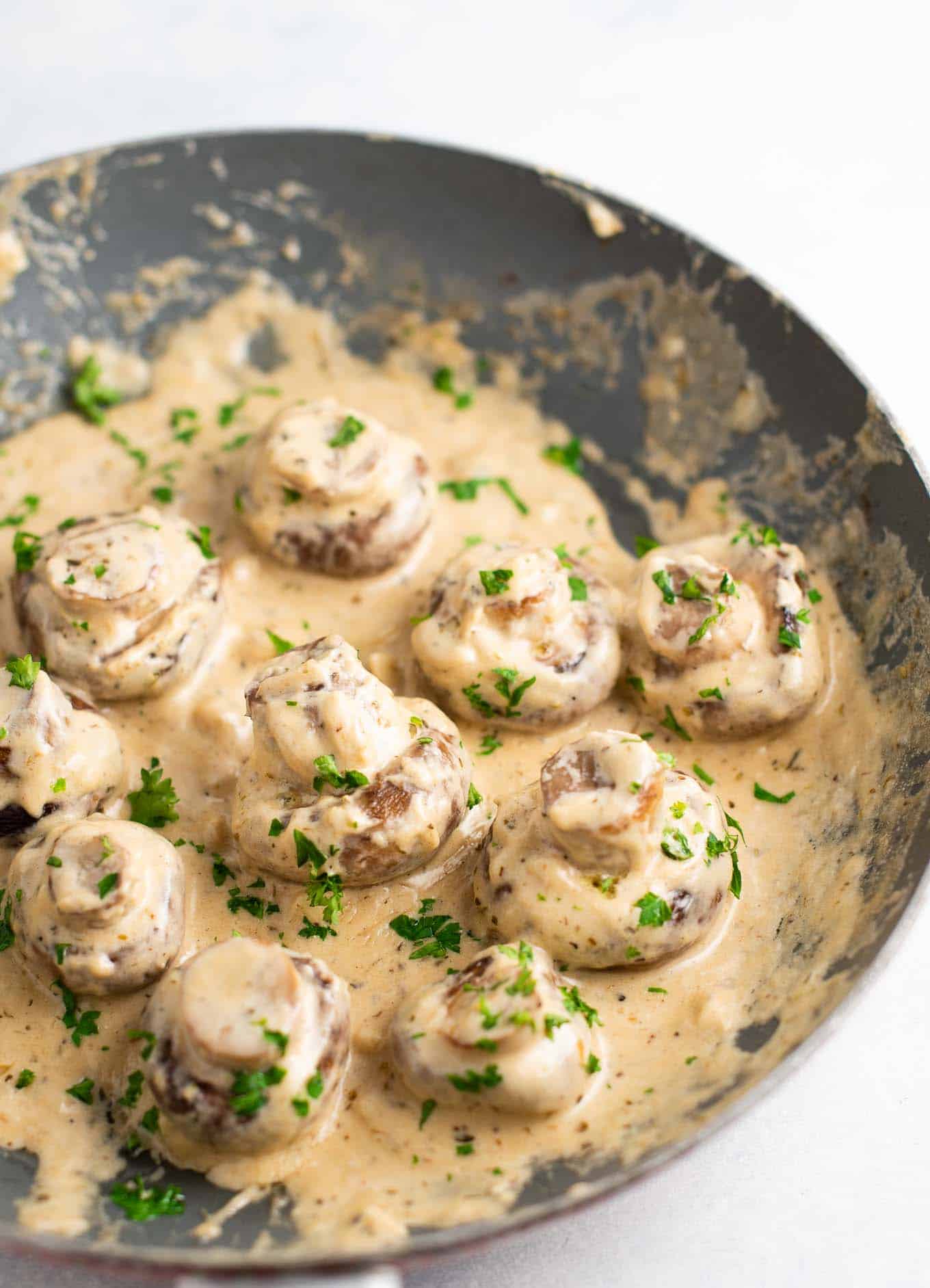 portobello mushrooms in cream sauce on a skillet sprinkled with fresh parsley