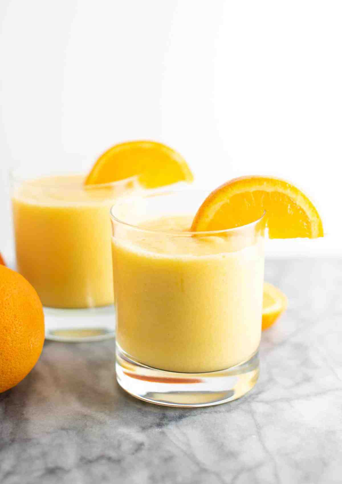 orange smoothie in a clear glass with a slice of orange on the rim