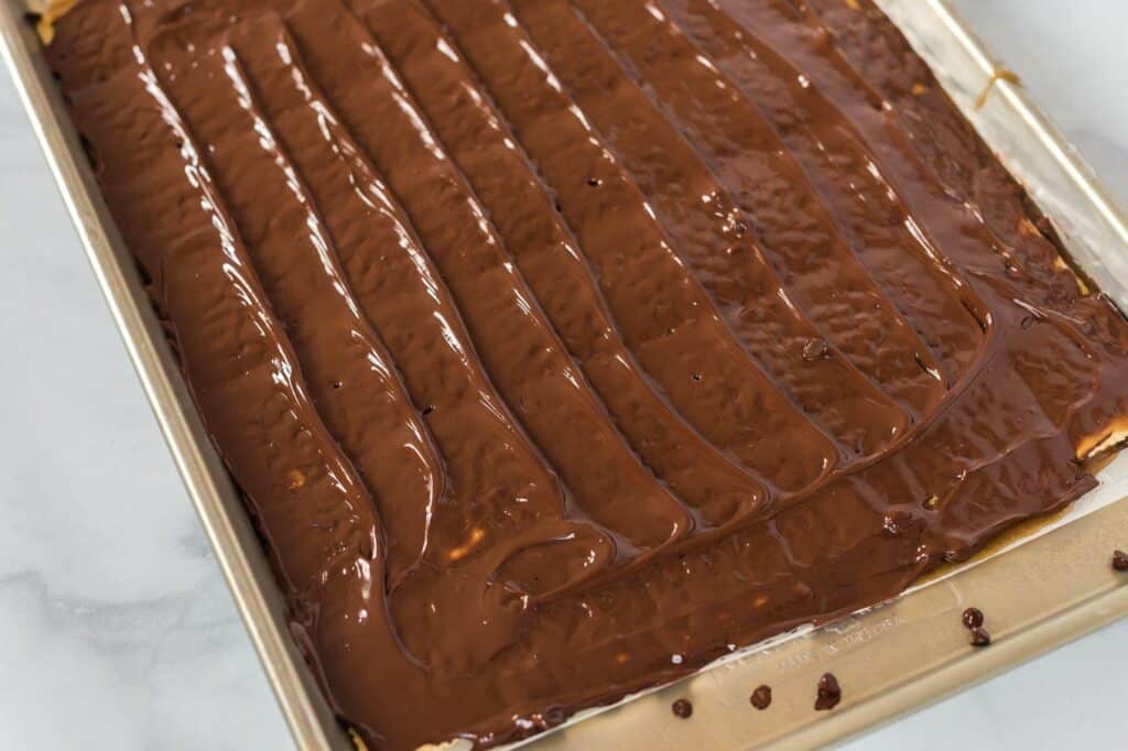 melted chocolate chips spread out over the saltine crackers on a baking sheet