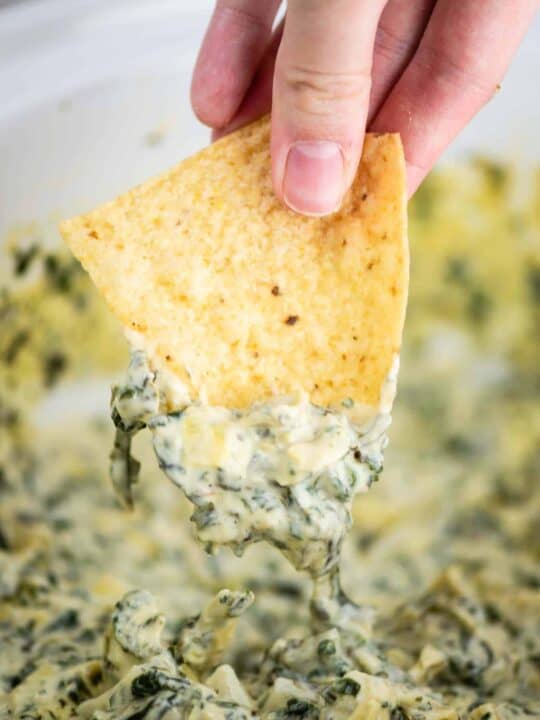 a chipped being dipped in spinach artichoke dip
